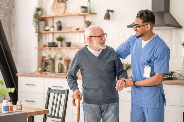A home care aide helping a client walk safely with a cane at home